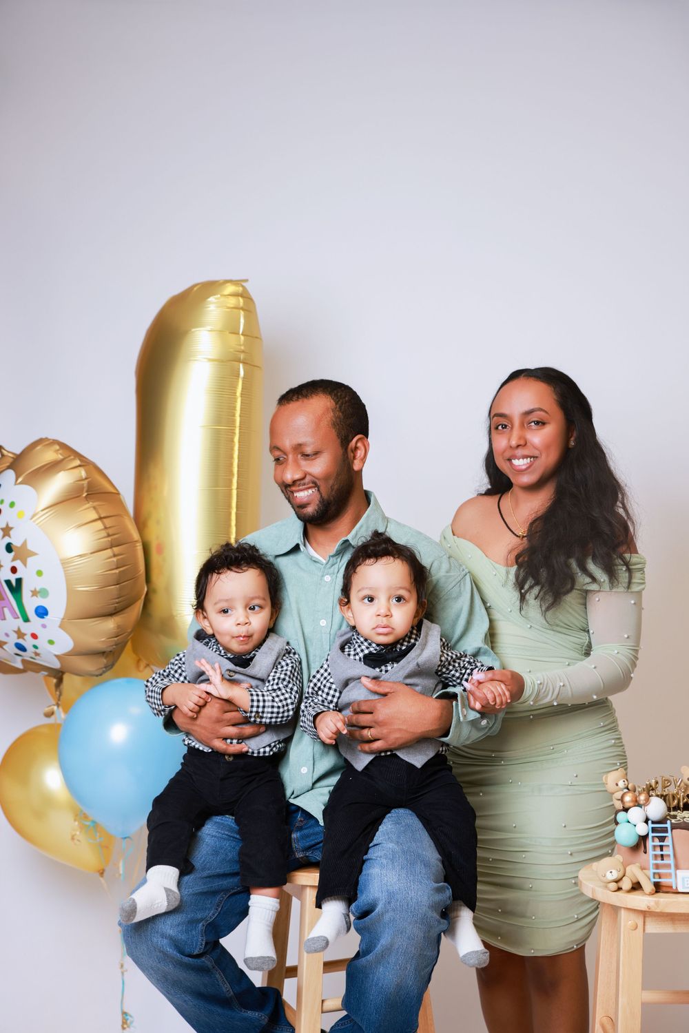 Family celebration setup with gold balloons and coordinated outfits against white background.