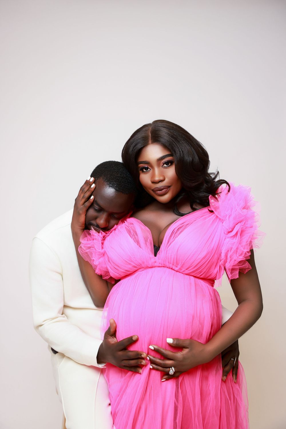 Maternity photoshoot featuring couple in white and bright pink outfits showing affection.