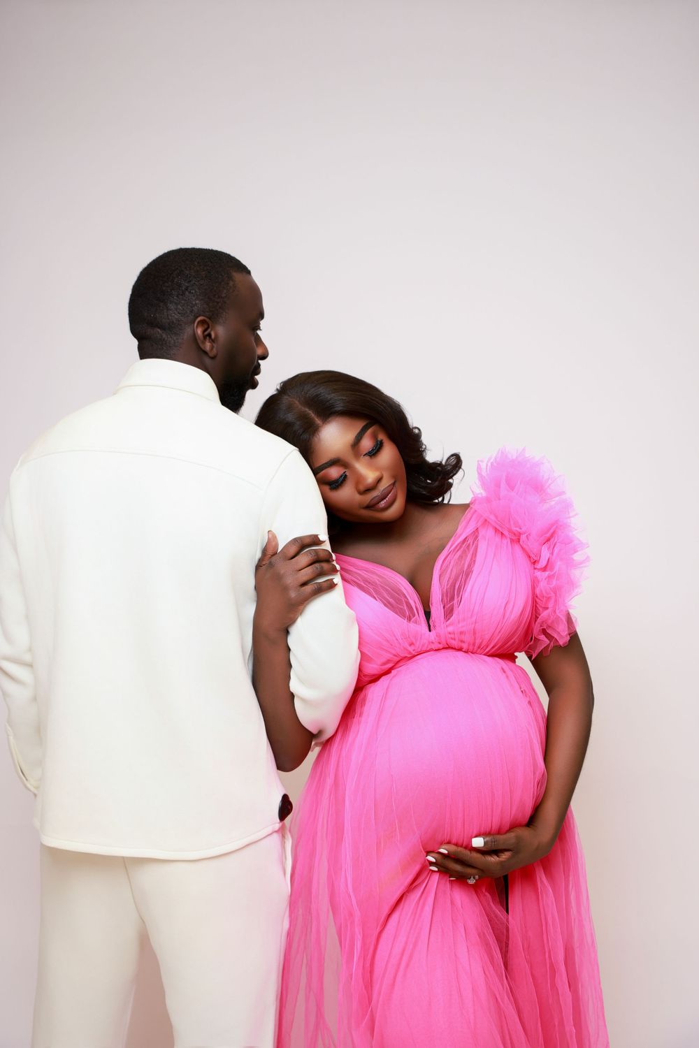 Intimate maternity photos of couple embracing, with person wearing vibrant pink tulle dress.