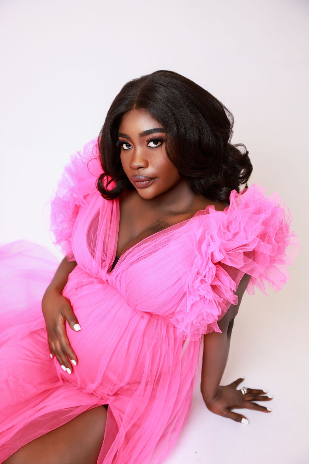 Elegant maternity photos featuring person in dramatic pink tulle gown with ruffled details.