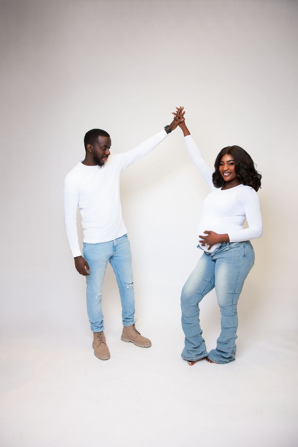 A couple in matching white sweaters and jeans share a celebratory high-five against a light background.