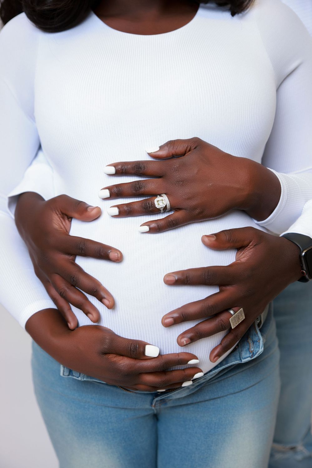 Close-up of hands cradling a pregnant belly, showing wedding rings and white manicured nails.