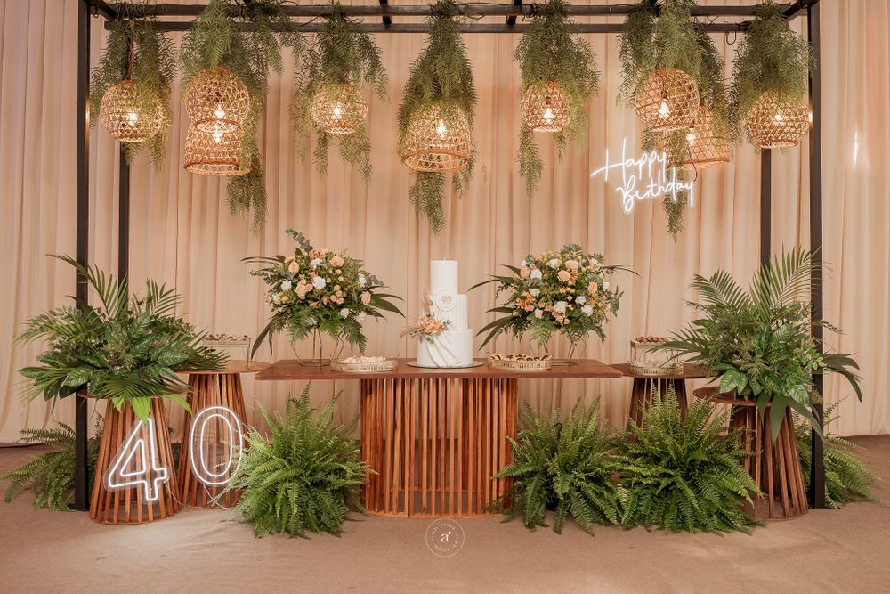 Event backdrop with illuminated 40 sign, suspended mason jar lights, and tropical greenery against draped fabric wall.