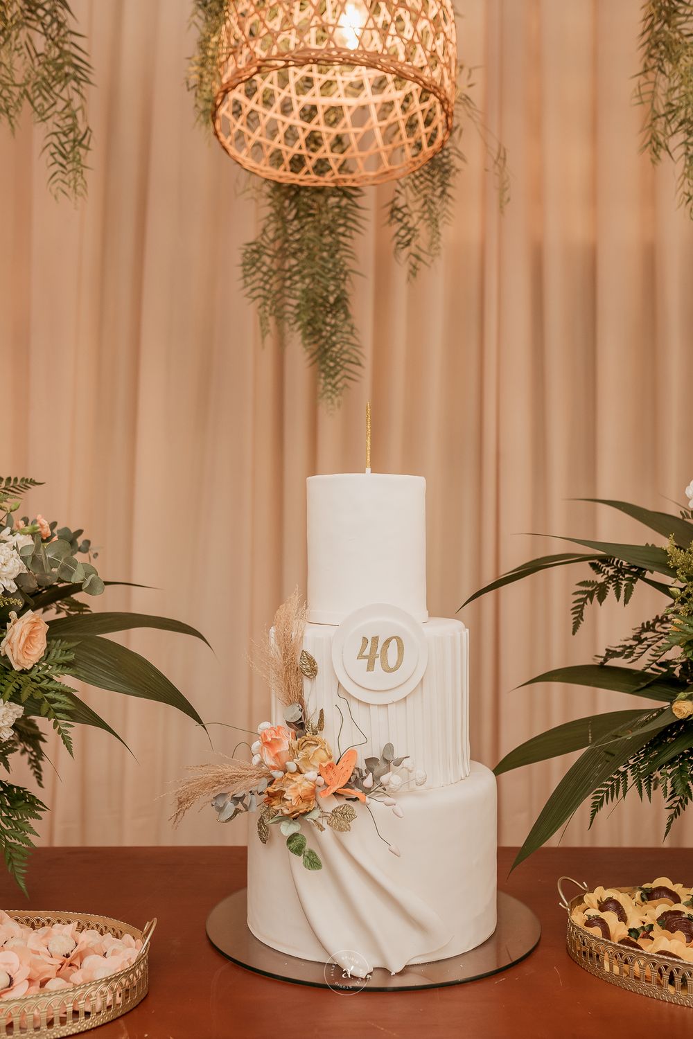 Elegant white tiered 40th anniversary cake with peach flowers and gold chandelier lighting in romantic setting.