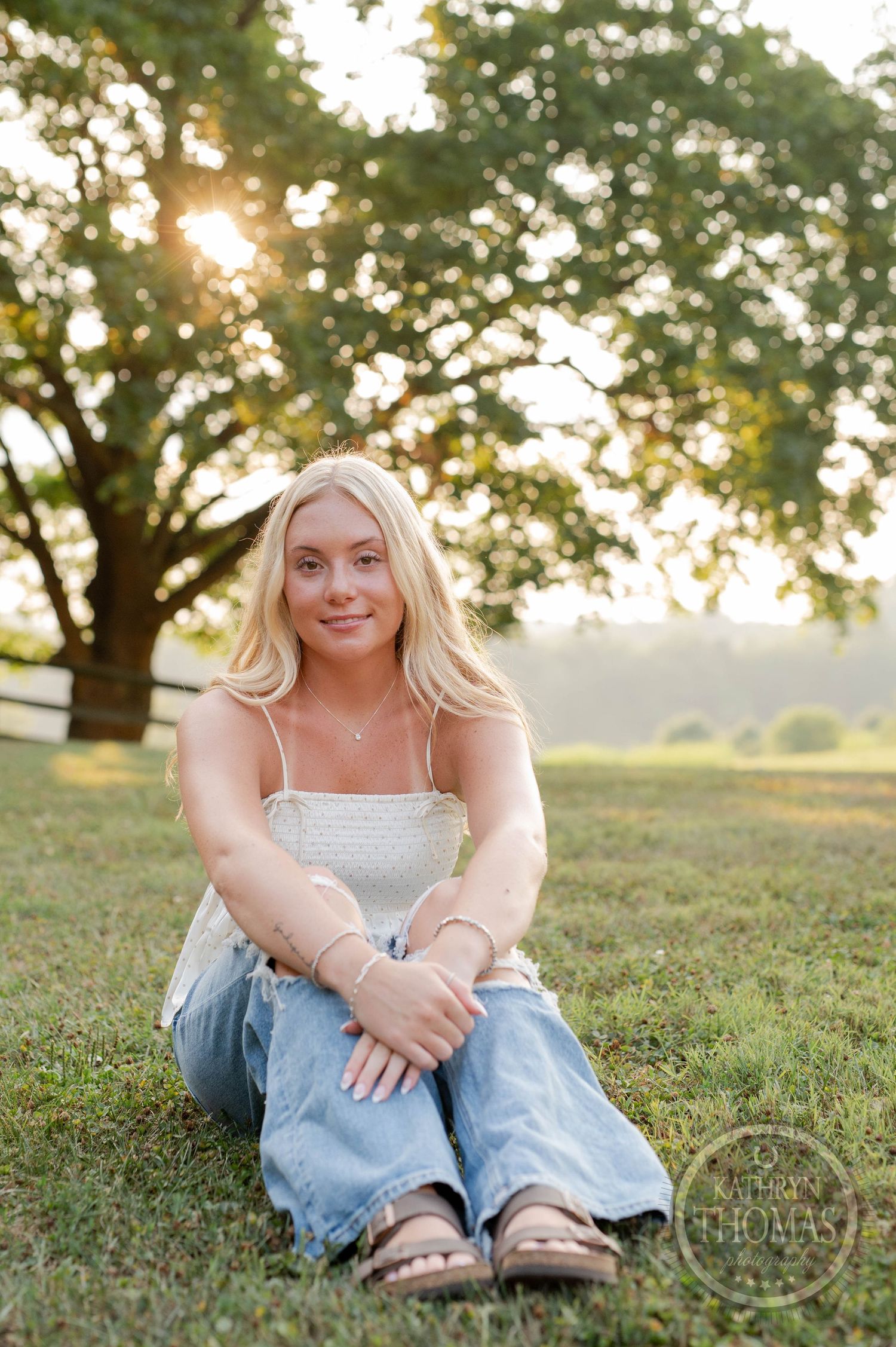 Casual outdoor portrait sitting on grass at sunset wearing distressed jeans and white top.