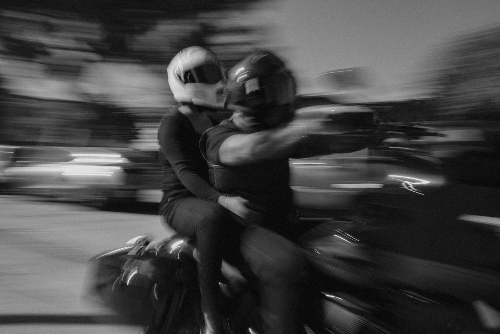 A black and white motion blur photograph showing a couple riding their motorcycle through Downtown Los Angeles, California.