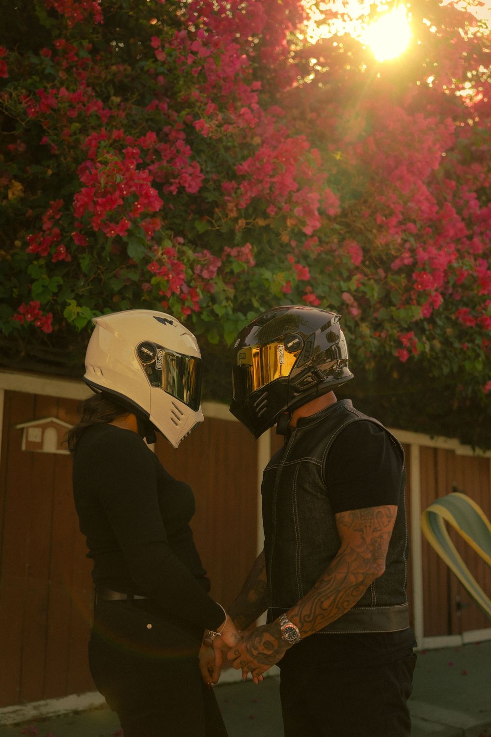 Two bikers in silhouette stand against a vibrant sunset with pink flowering trees in the background in Los Angeles, California.