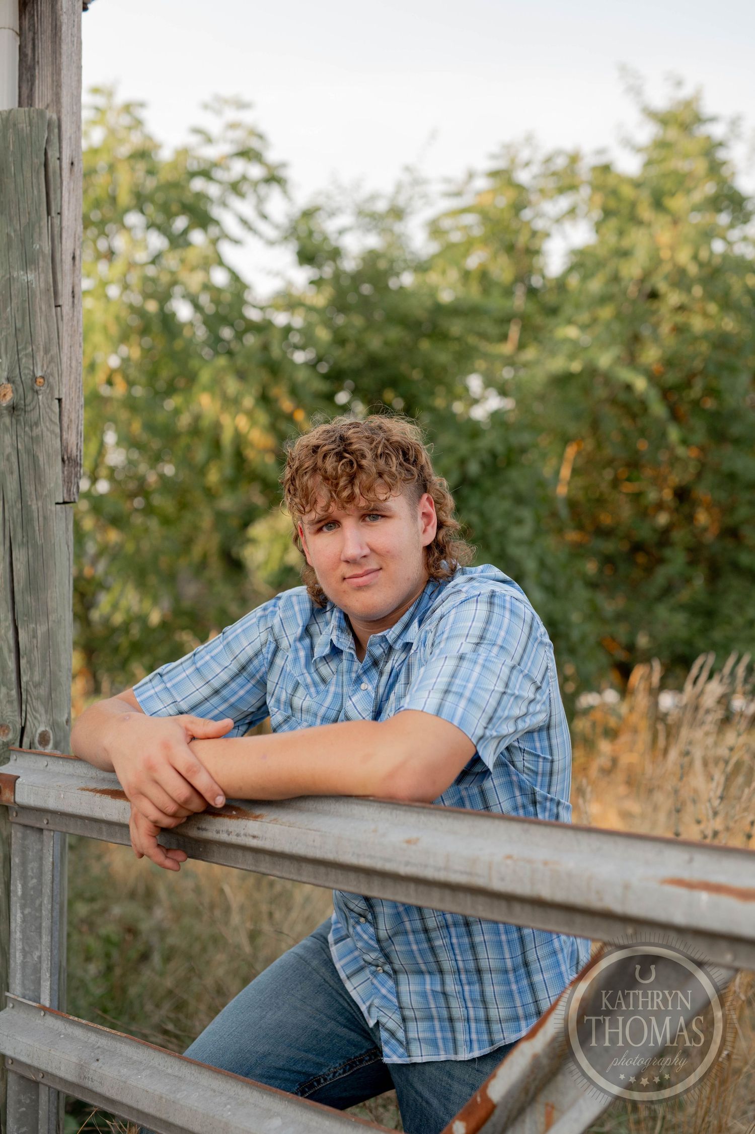 A summer portrait leaning on a wooden fence rail during golden hour lighting.