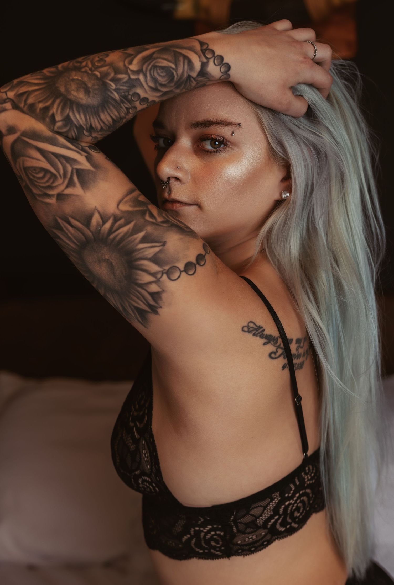 Artistic boudoir photo of a woman with floral arm tattoos and platinum hair posing in black lingerie.
