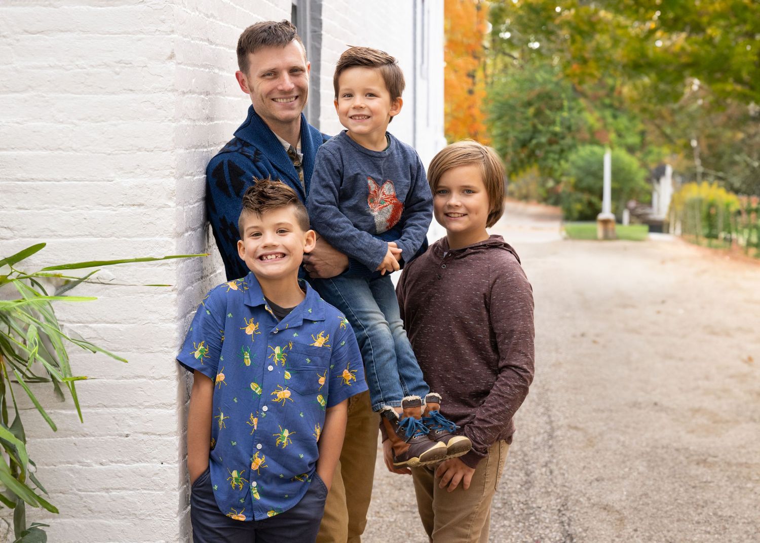 Dad with three sons embracing and smiling against white brick wall in Worthington Ohio, by Jamie Macey Photography
