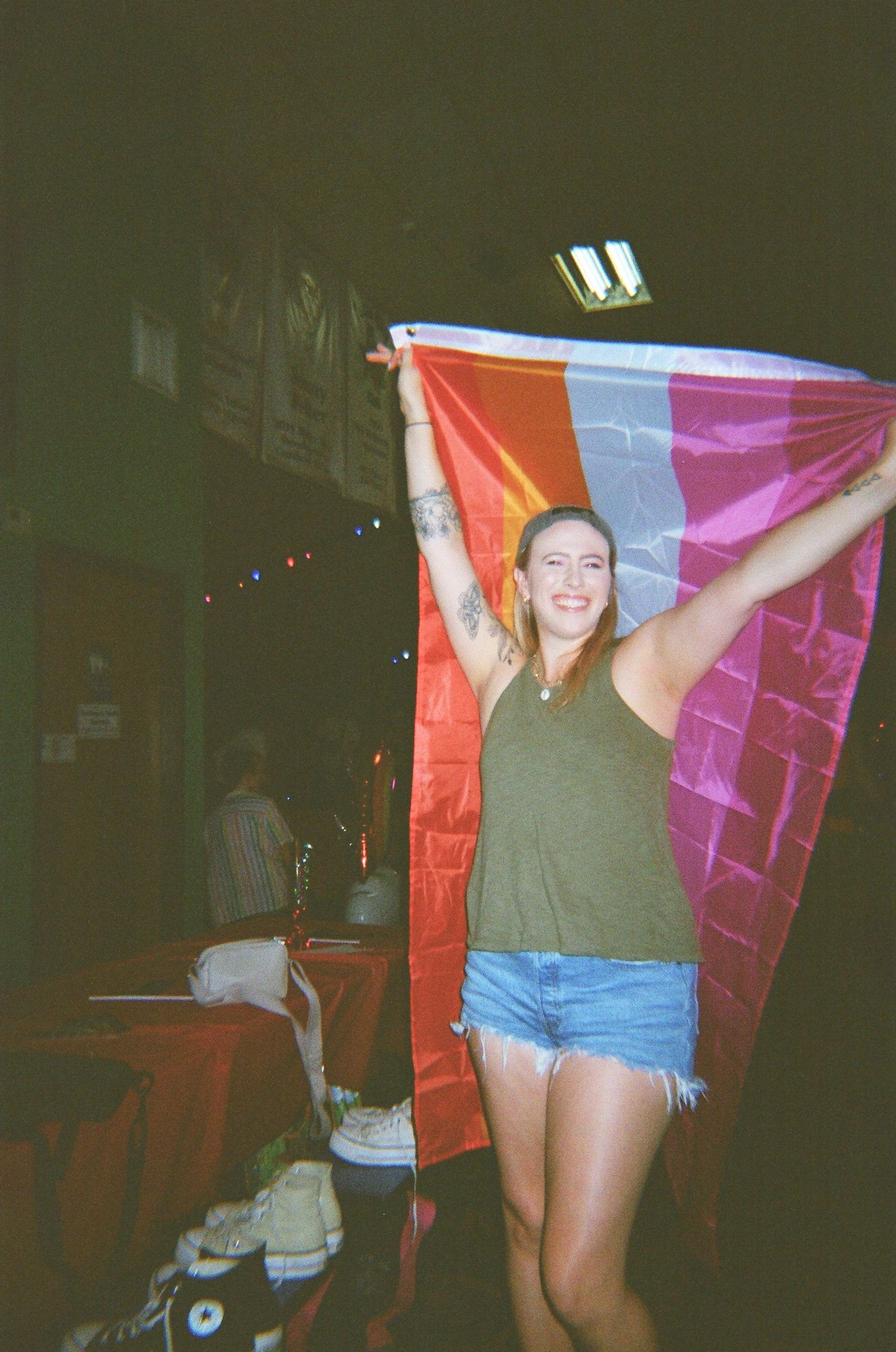 Person holding up colorful pride flag in dimly lit indoor setting.