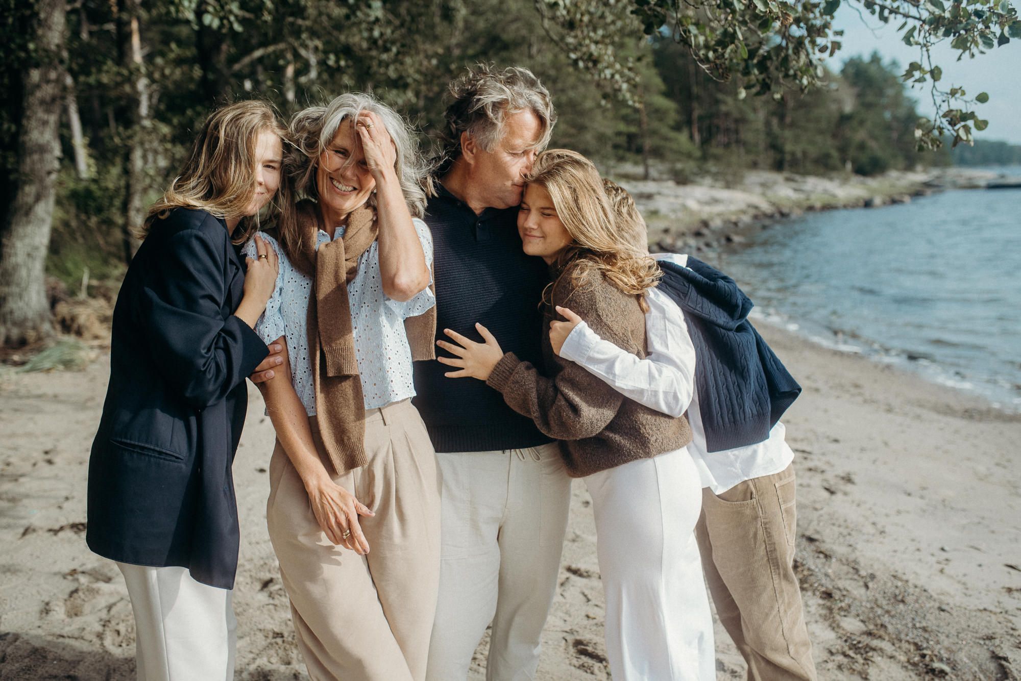 Friends sharing intimate moment on beach with ocean and forest background.