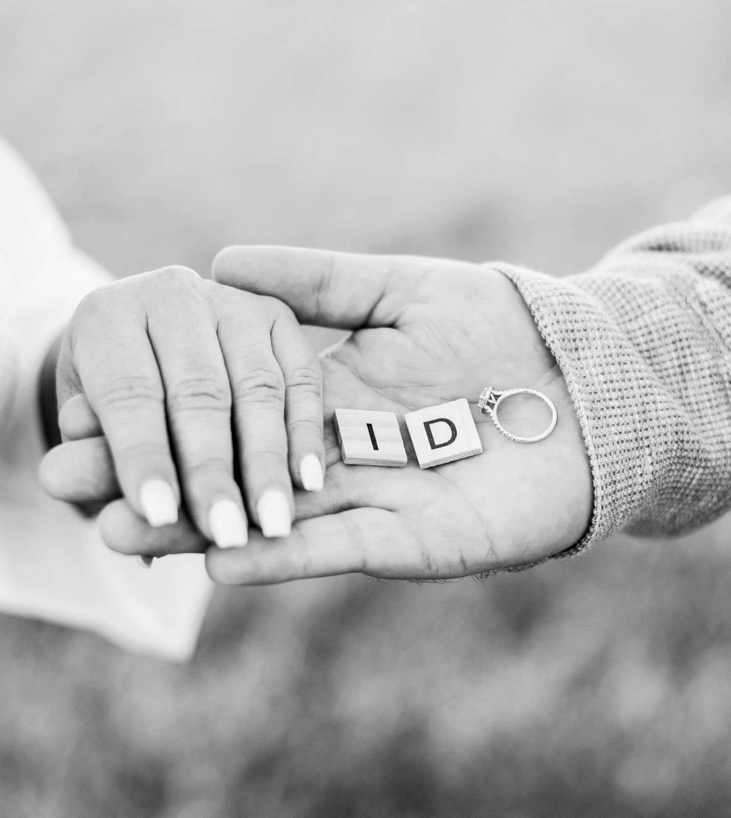 Close-up black and white photo of hands holding letters spelling out 'I DO' against a blurred background.
