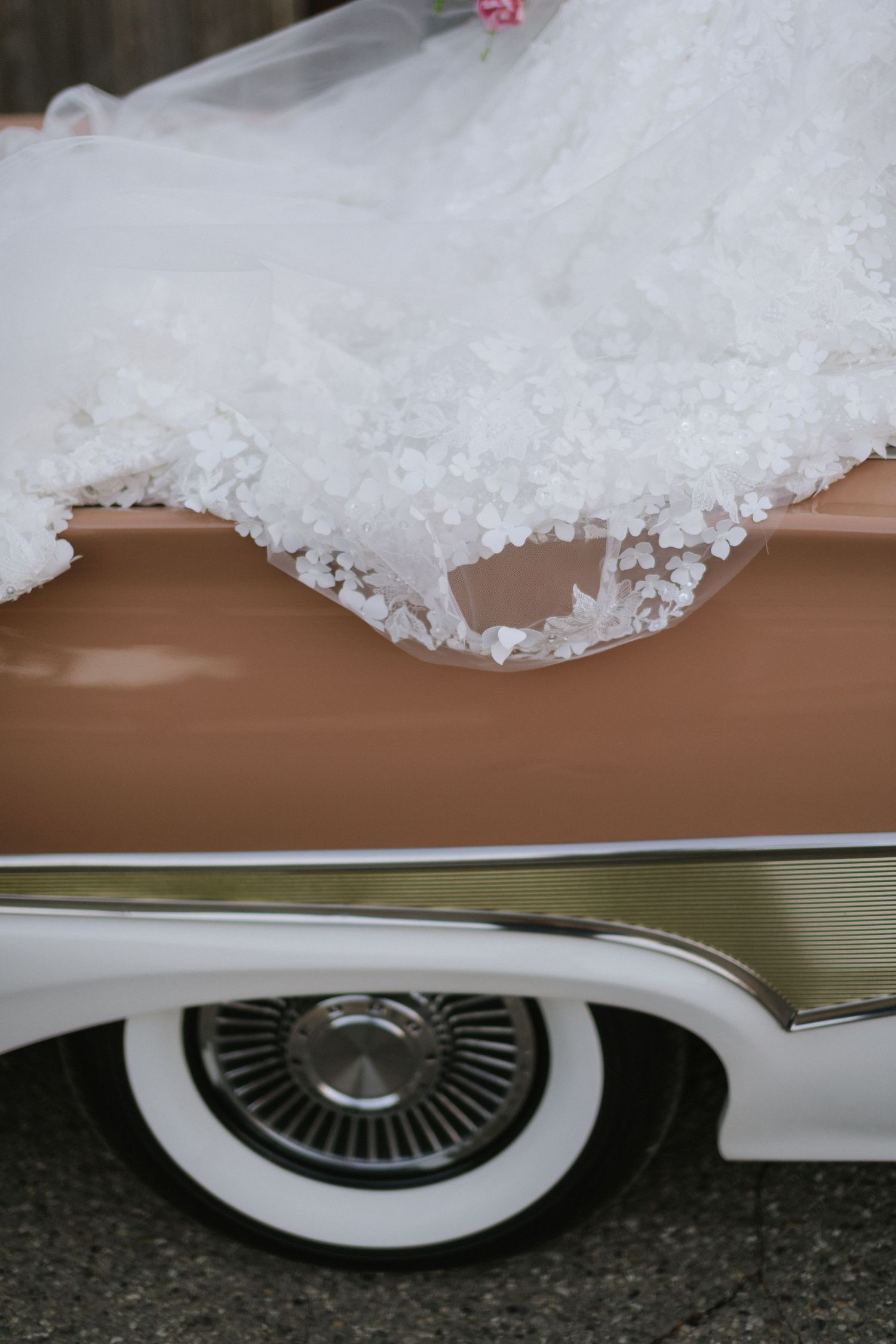 White lace wedding dress detail draped over a classic car with whitewall tires.