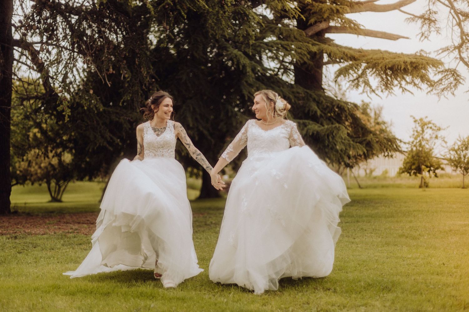 Photographe mariage Auvergne Rhône-Alpes – couple de femmes dansant dans un champ au coucher du soleil au Château de Féligonde.