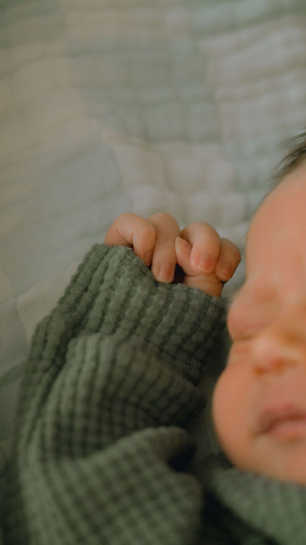 Close-up detail of tiny fingers grasping a green knit sweater sleeve.