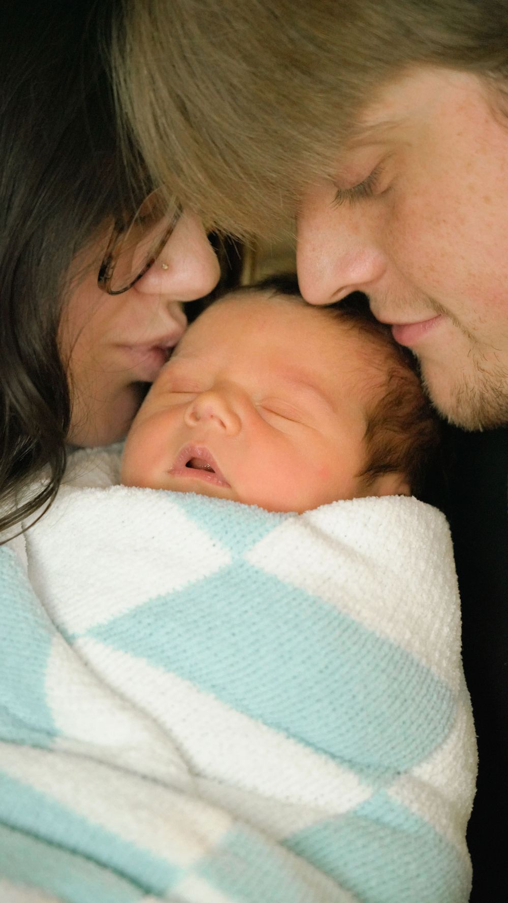 Newborn baby wrapped in blue and white striped blanket being cradled with tenderness.