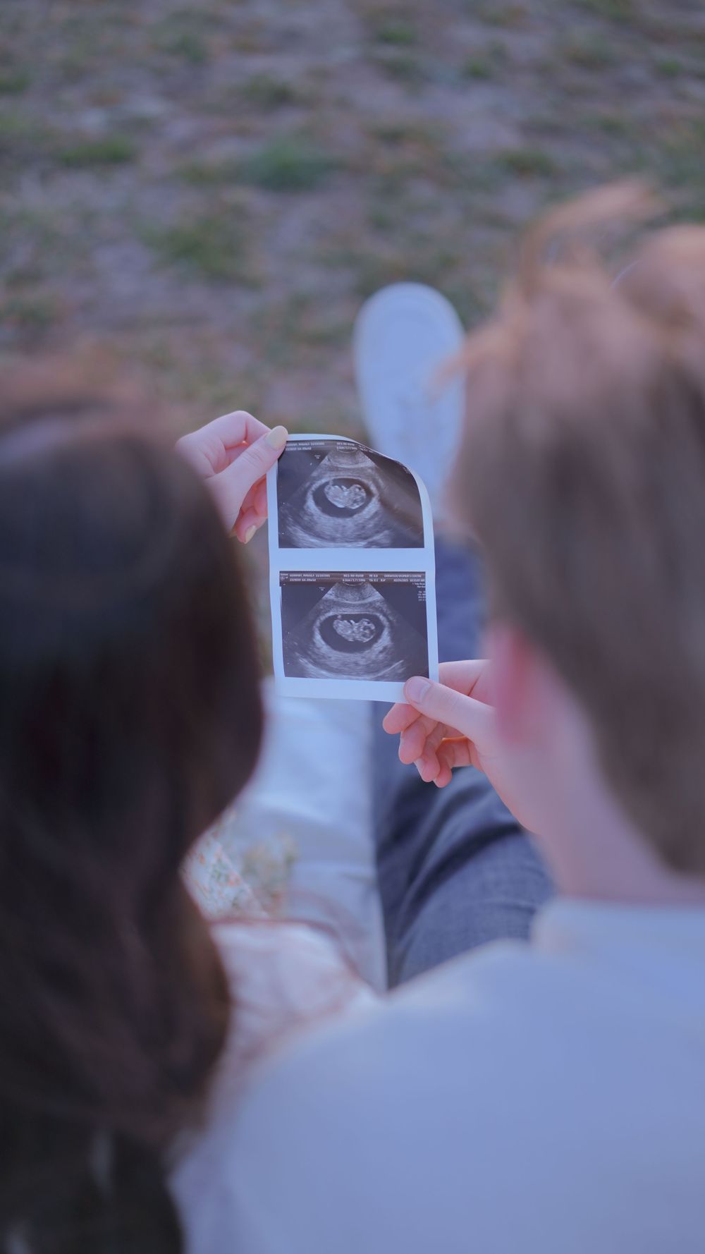 Two people looking at ultrasound sonogram images together while sitting outdoors.