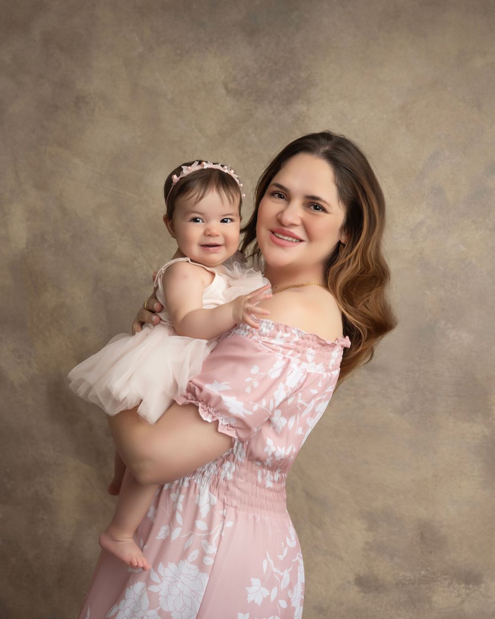 A tender family moment captured in pink tones showing playful interaction against a textured brown backdrop.
