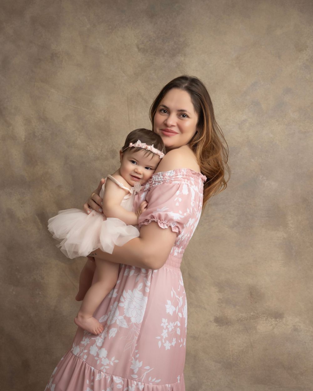 Joyful family portrait in coordinating pink outfits against a neutral studio background.