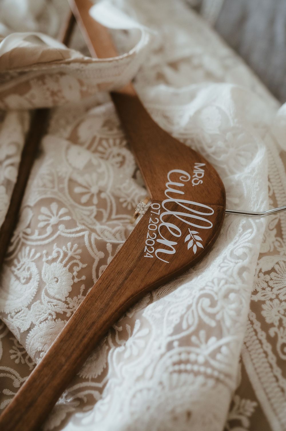 Wooden spoon with delicate lace details and custom engraving resting on white lace fabric.