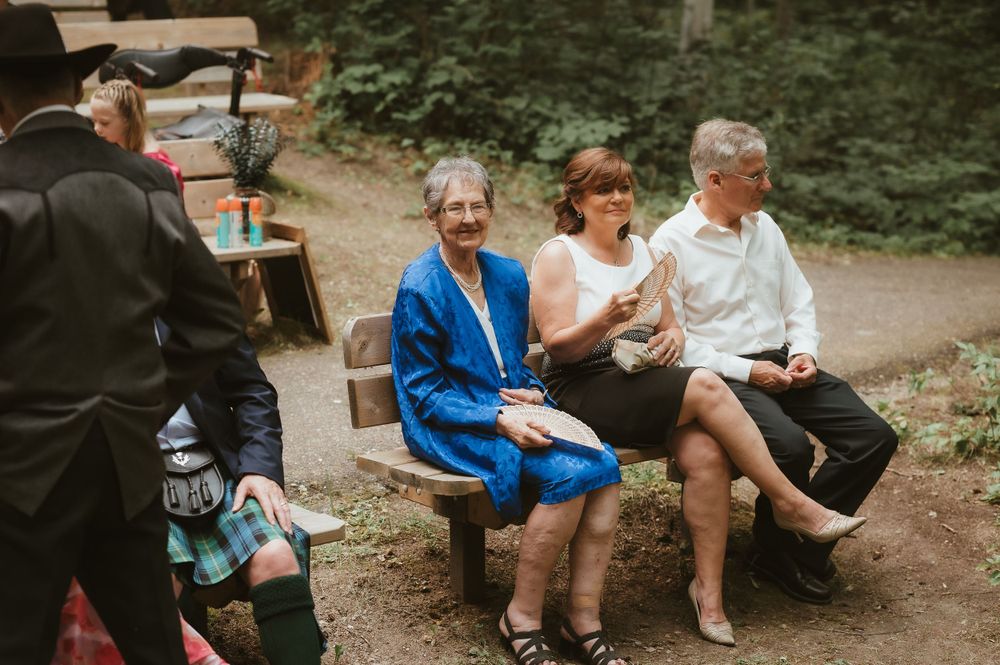 Wedding guests sitting on wooden benches in an outdoor setting.