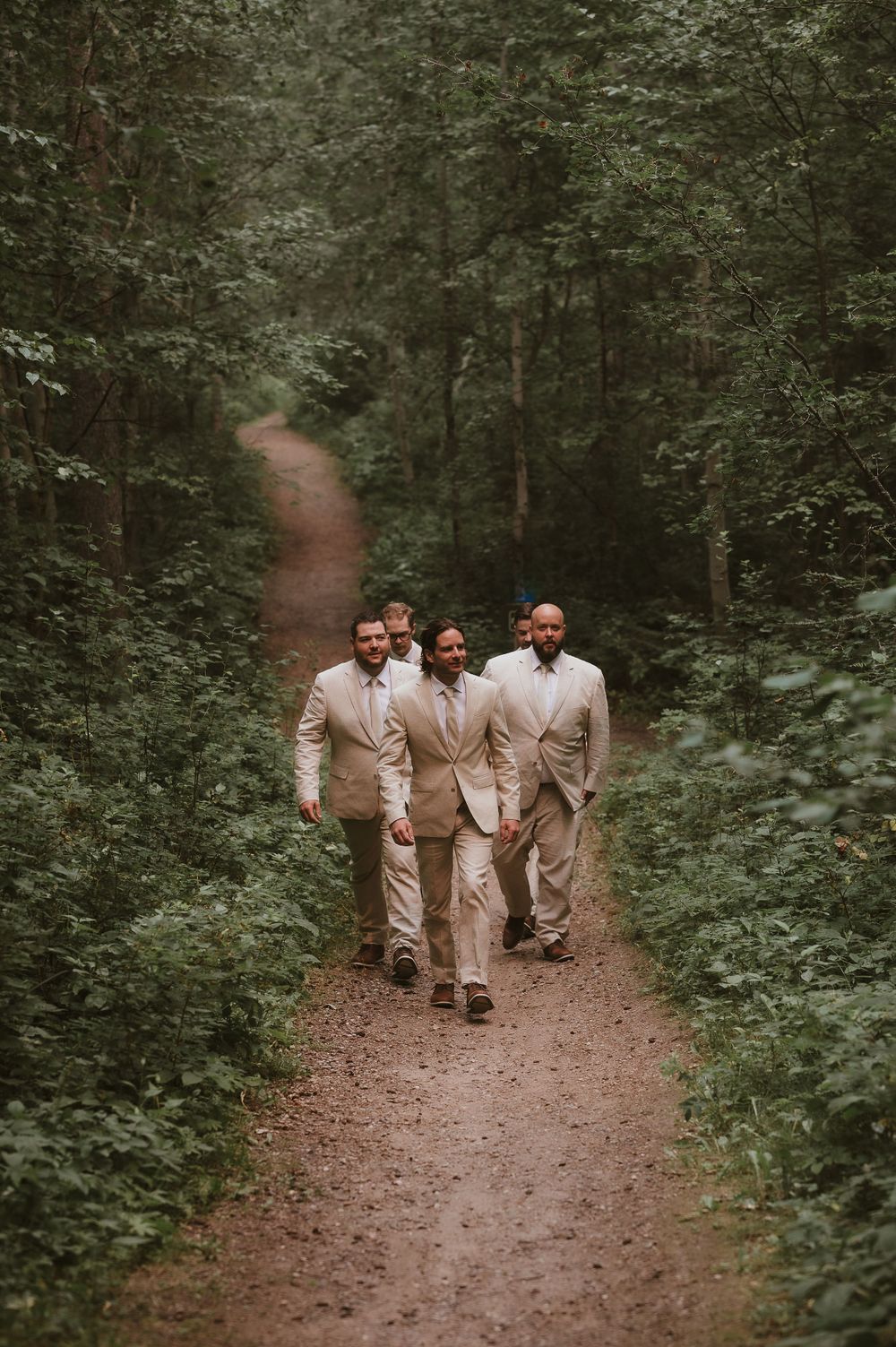 Three people in beige suits walking down a wooded trail.