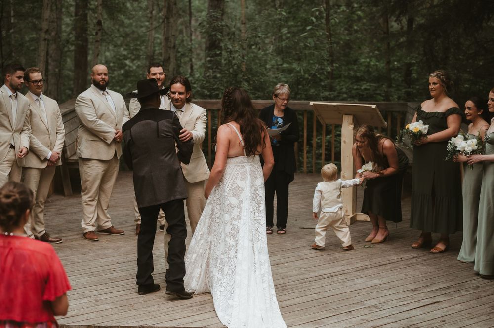 Intimate forest wedding ceremony with couple exchanging vows surrounded by wedding party.