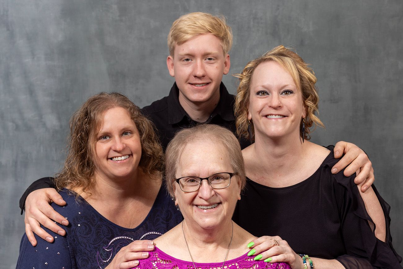 Studio portrait of four people smiling together against a grey background.