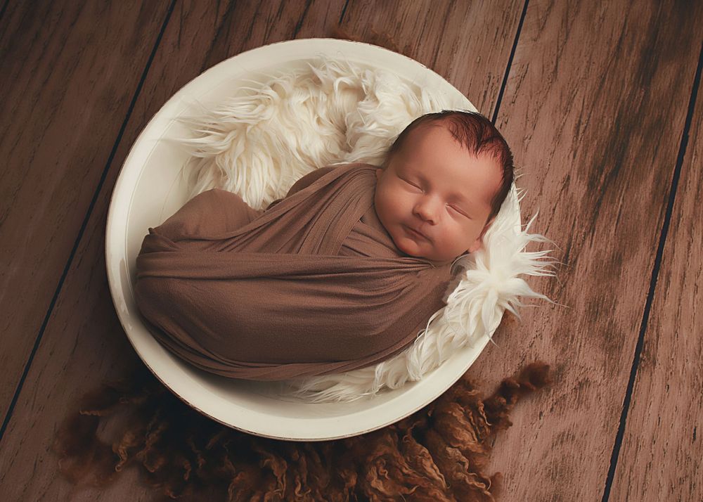 A peaceful newborn baby boy wrapped in soft fabrics, captured in a serene and intimate setting, showcasing the delicate beauty of early life