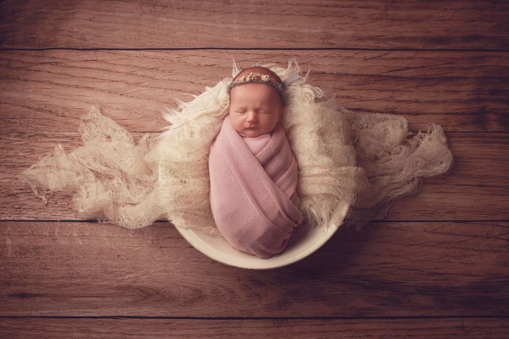 A peaceful newborn baby girl wrapped in soft fabrics, captured in a serene and intimate setting, showcasing the delicate beauty in photo