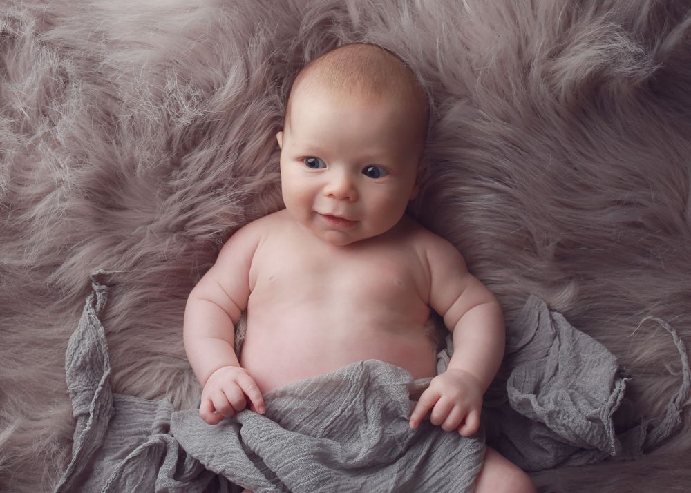 A cheeky baby boy flashing a playful smile, capturing his adorable personality joyful spirit during a fun and lively newborn photo session