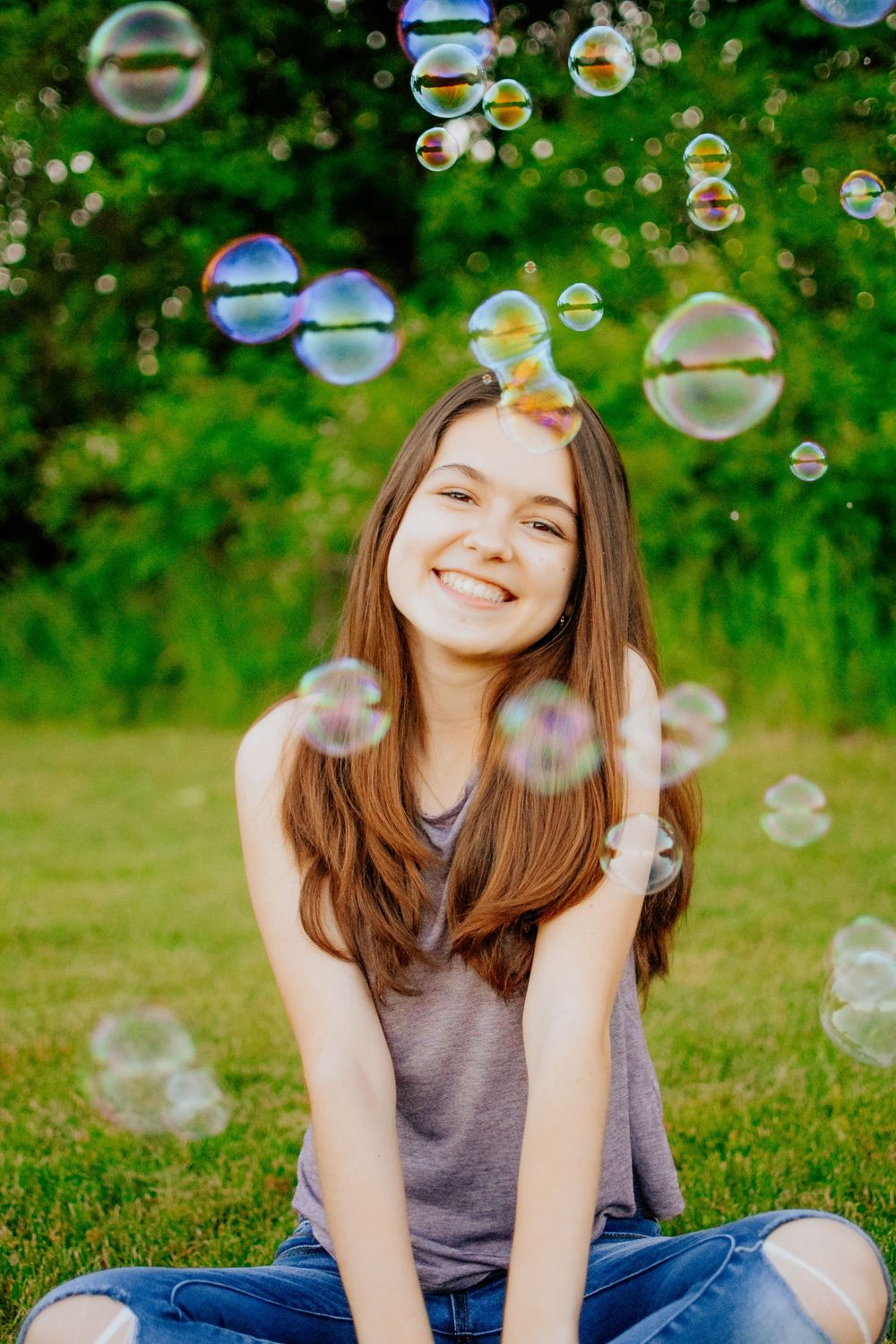 A girl sitting cross-legged and smiling with bubbles passing her face.