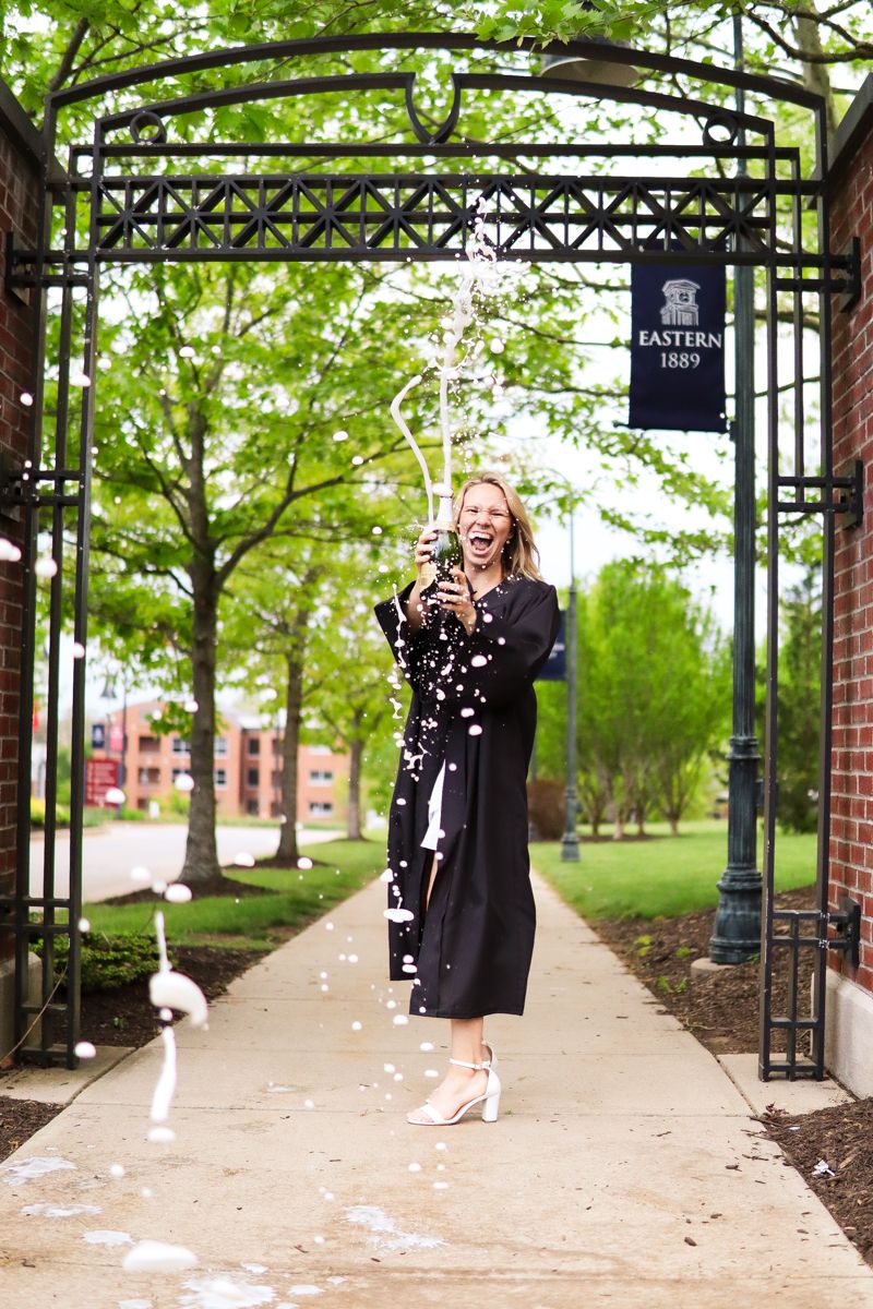 Girl popping champagne at her college campus during college graduation photos.