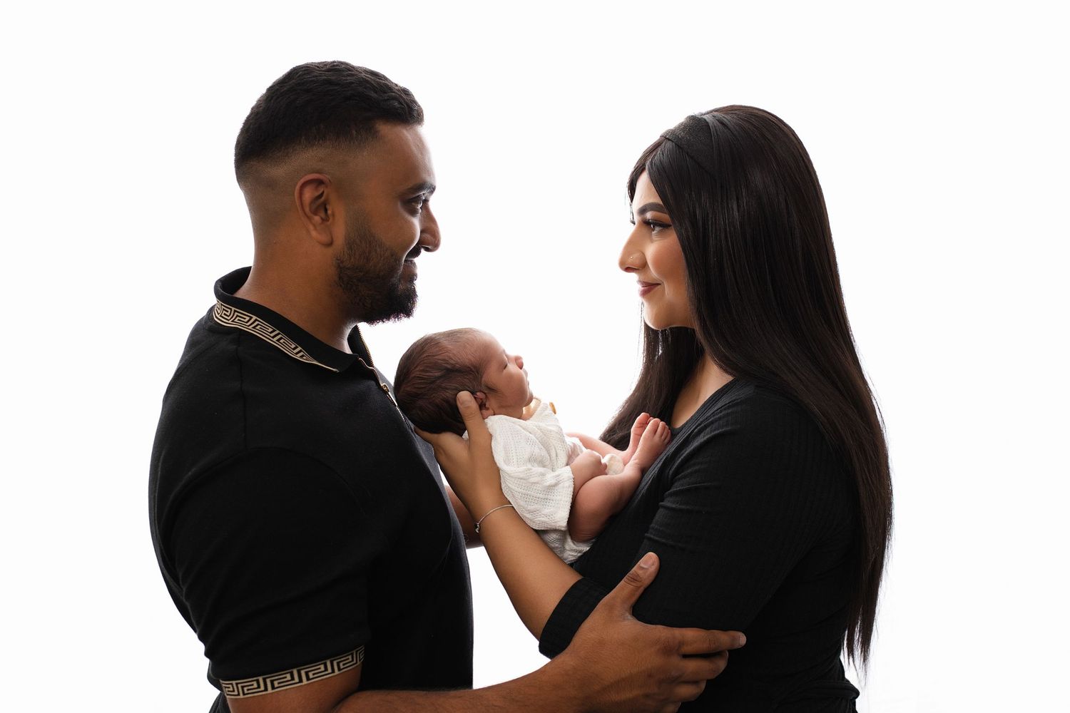 Two parents lovingly holding their newborn baby against a white studio background.