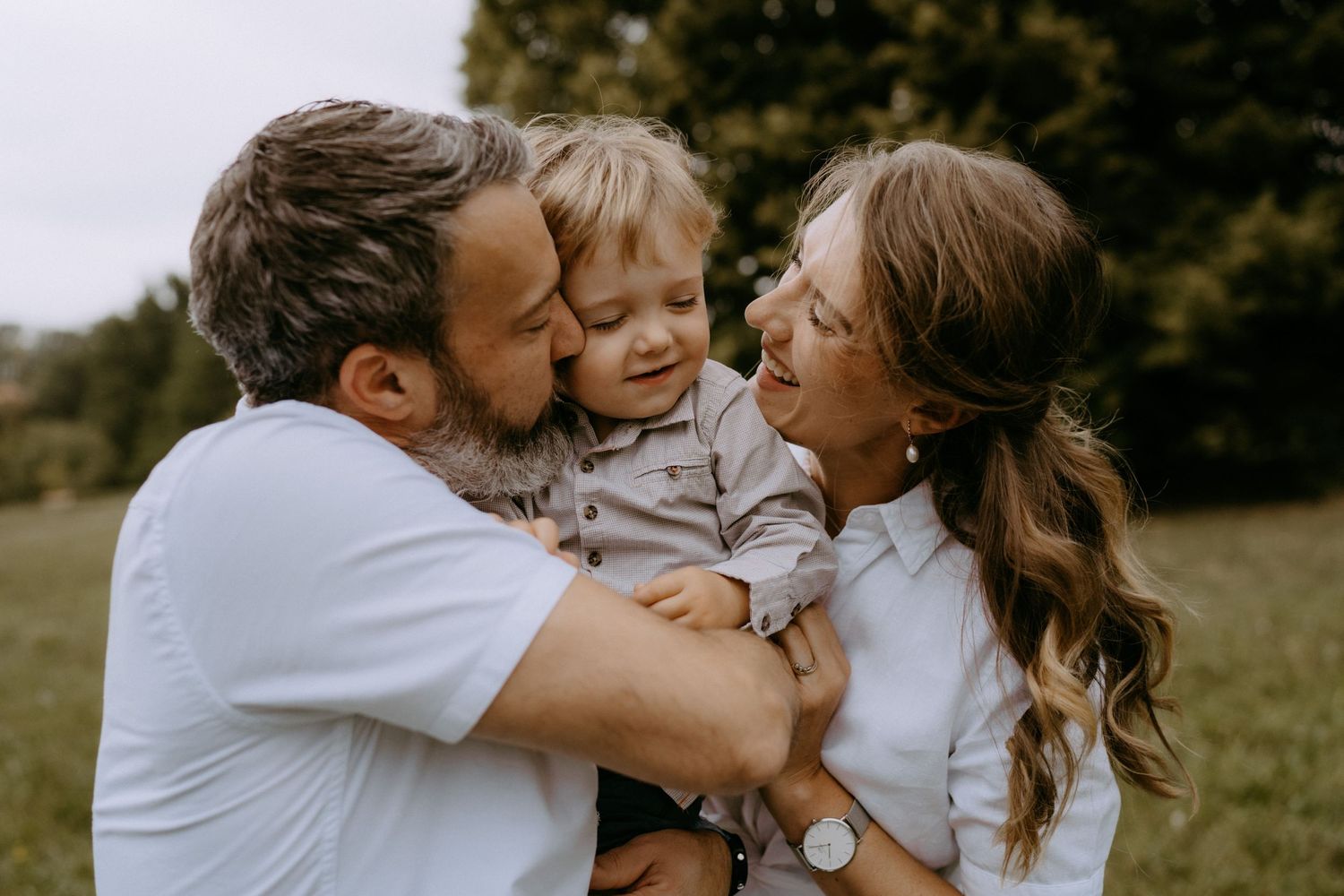 A family shares joyful embraces and laughter in a sunny outdoor field.