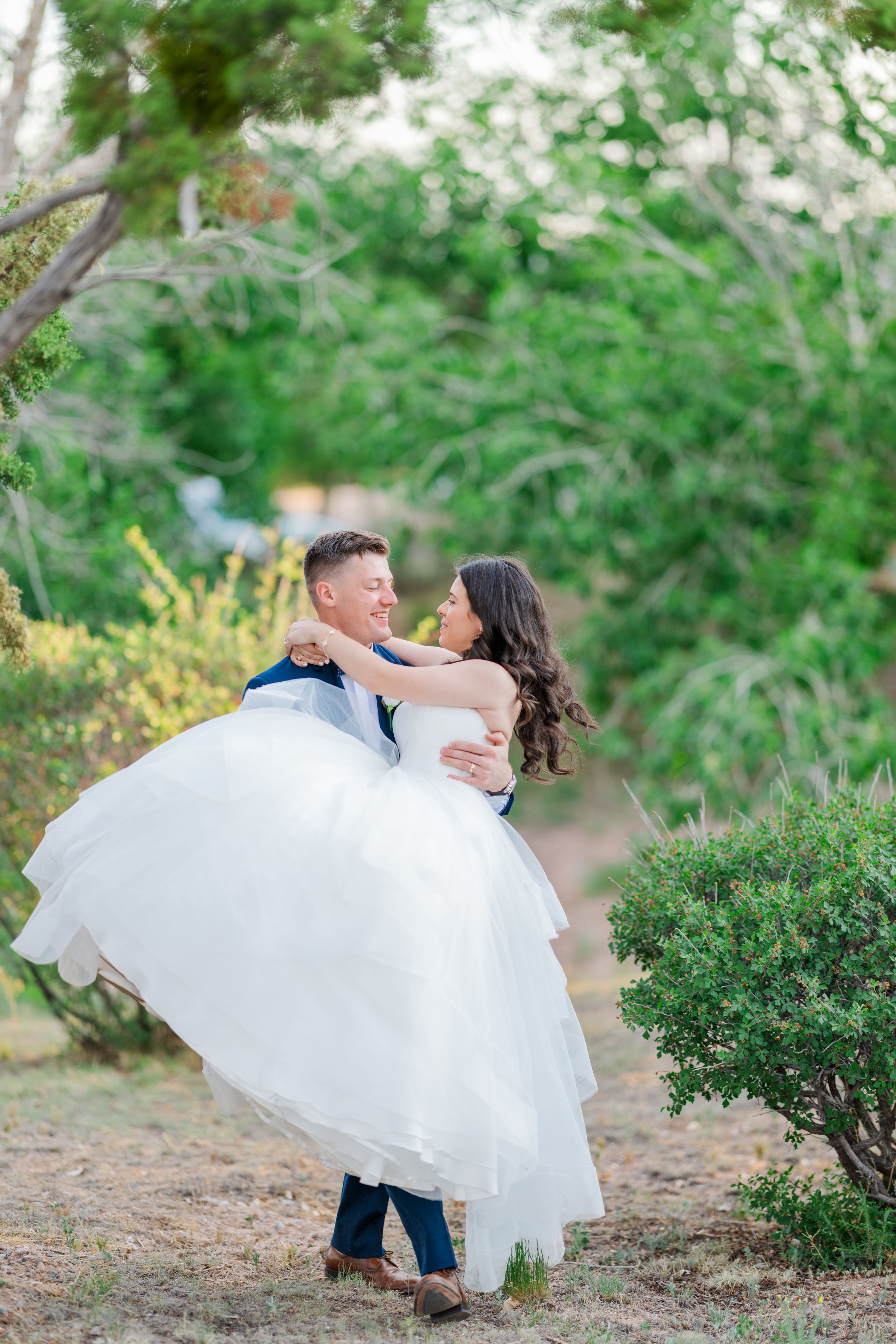 A couple shares a romantic moment in a garden setting as the groom carries the bride in her flowing white dress.