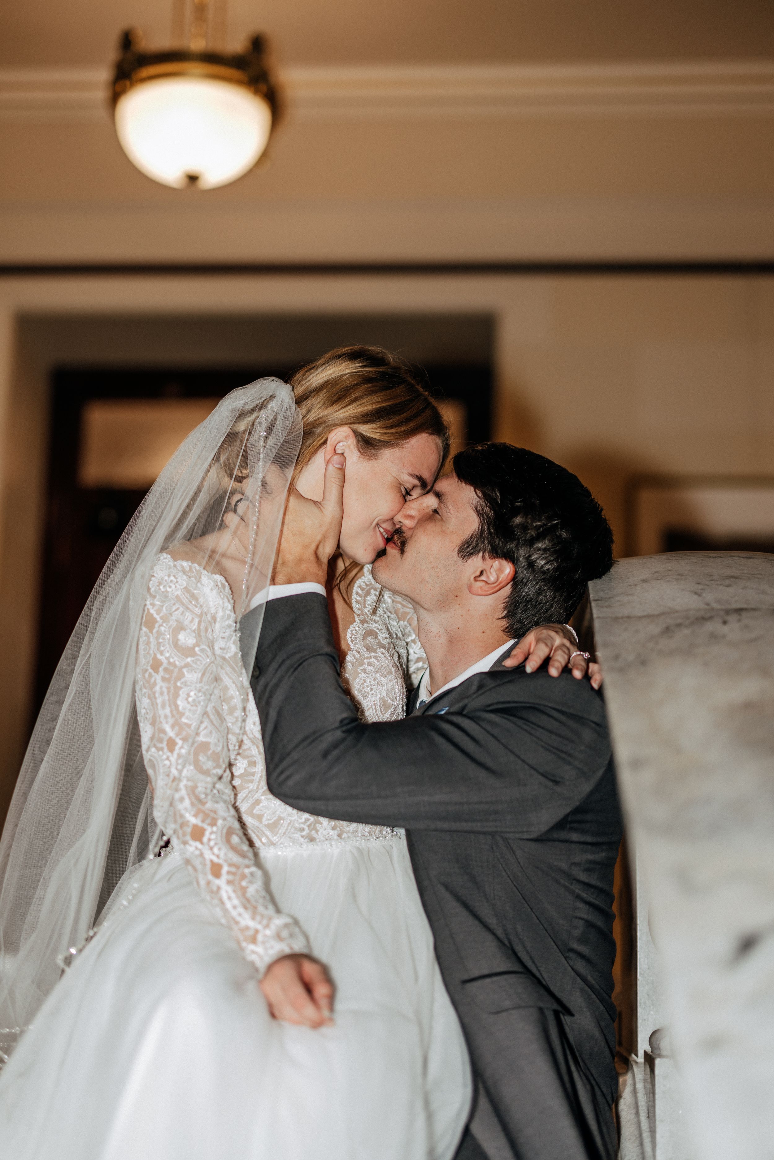 A tender moment between newlyweds sharing their first kiss in a softly lit room during their wedding celebration.
