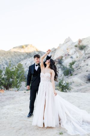 A bride and groom share a romantic dance moment in a desert landscape with rocky mountains in the background.