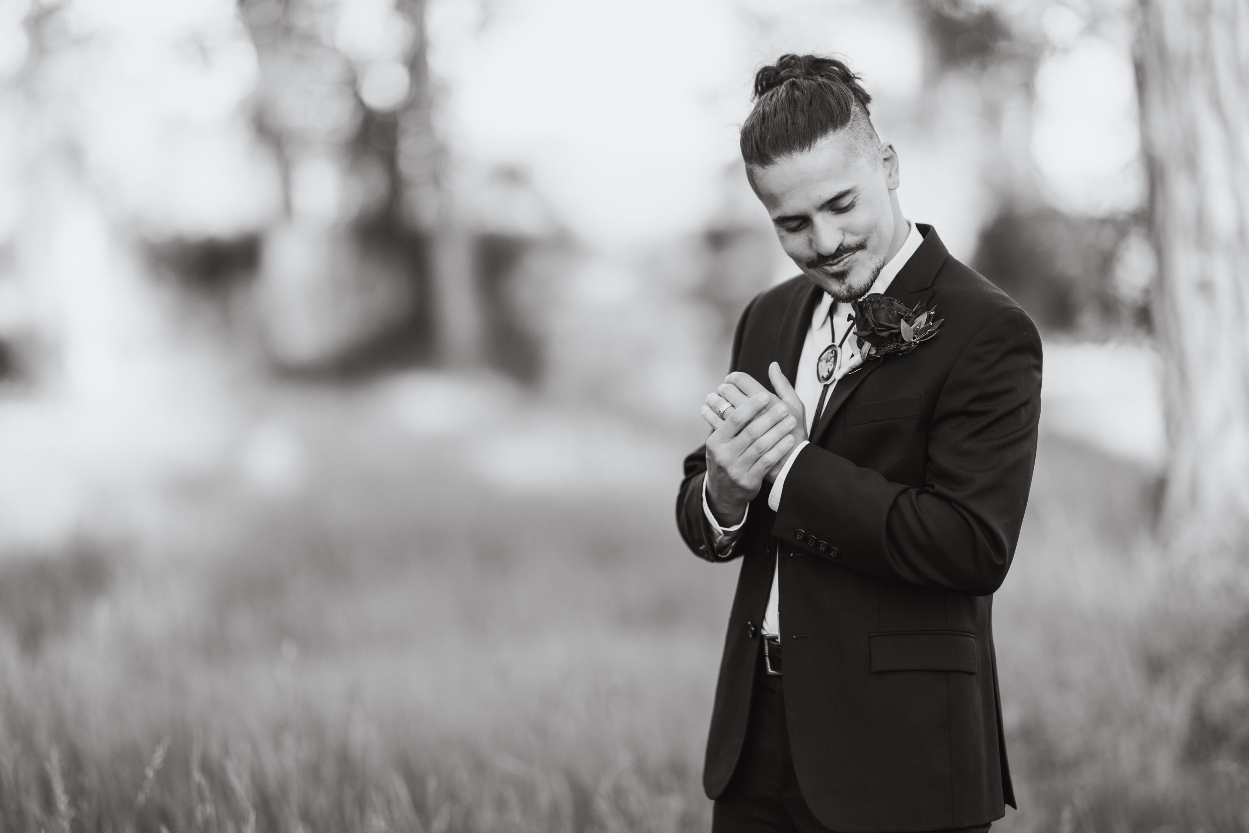 A black and white photo of someone in a suit looking down at a phone with a smile on their face in an outdoor setting.