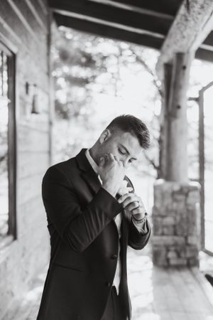 A black and white photo of someone in a suit lighting a cigarette on a covered porch.