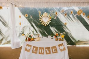 A rustic wedding table with LOVE banner, white tablecloth, and gold sunburst decorations under a white tent.