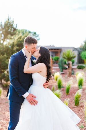 Bride and groom share a romantic kiss in a desert garden setting with palm trees and desert landscaping.