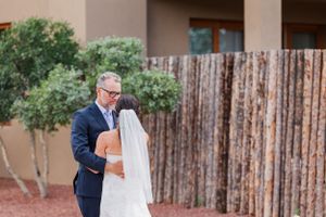 A couple shares a romantic moment in front of a rustic fence wall at a Southwestern style venue.