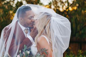 A romantic wedding moment captured under a flowing veil at sunset with warm golden lighting in the background.