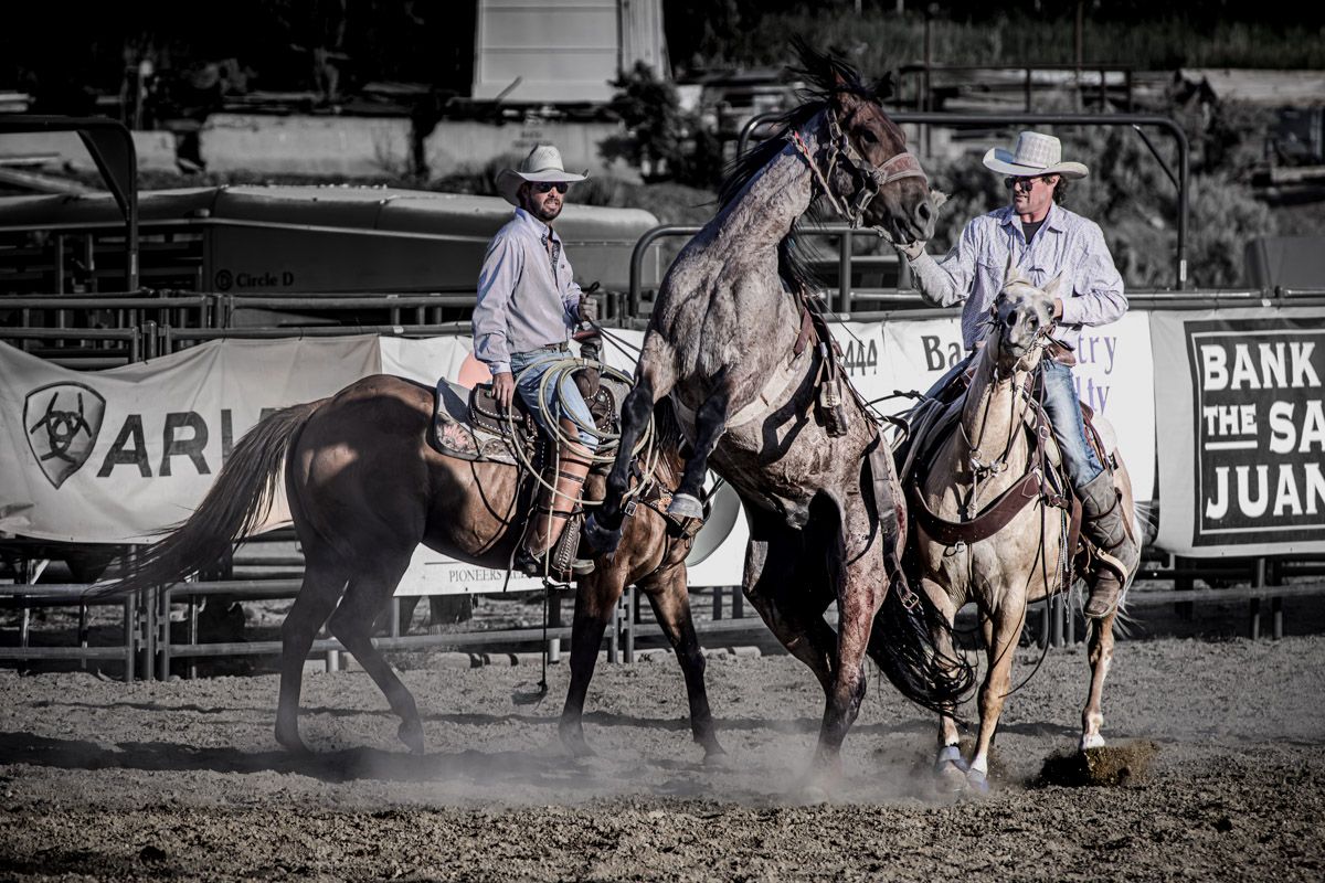 Western riders on horseback competing in rodeo arena.