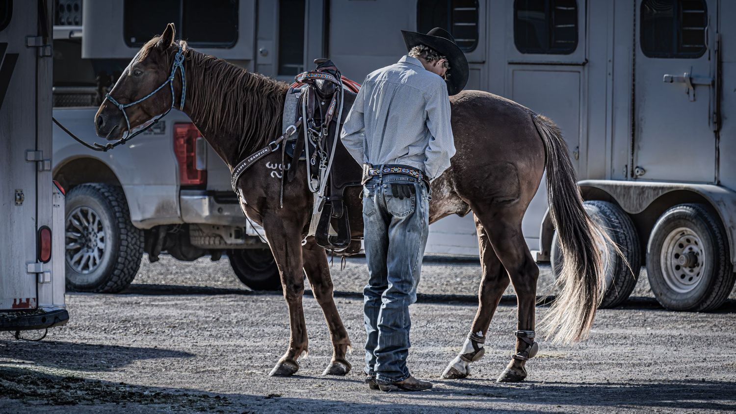 Horse and rider near trailer in black and white western scene.