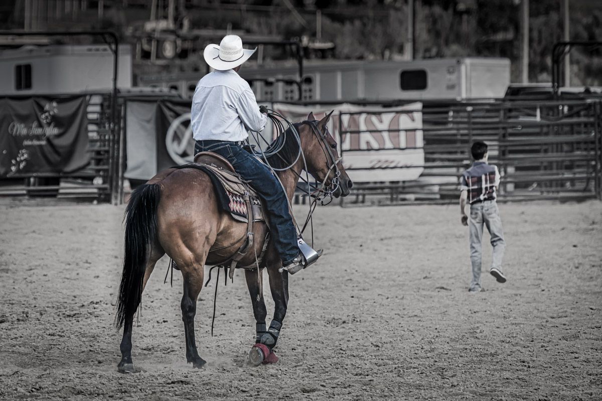 A rider on horseback practices in a dusty rodeo arena.