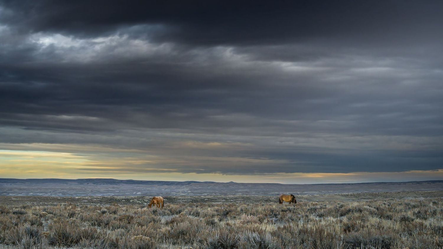 A dramatic stormy sky over a vast western landscape with mountains in the distance.