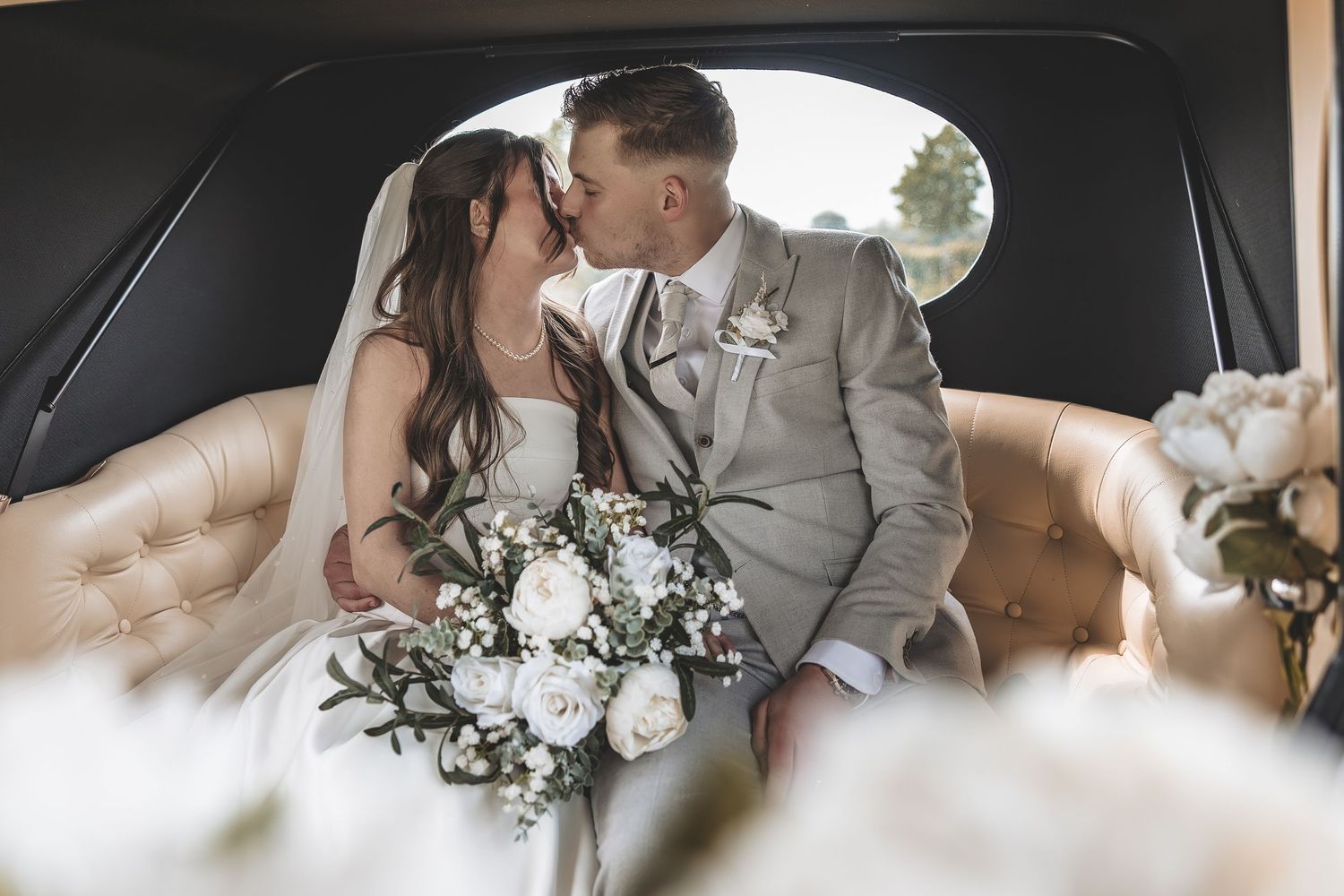 A genuine wedding couple moment sharing a kiss in the back of their wedding car.